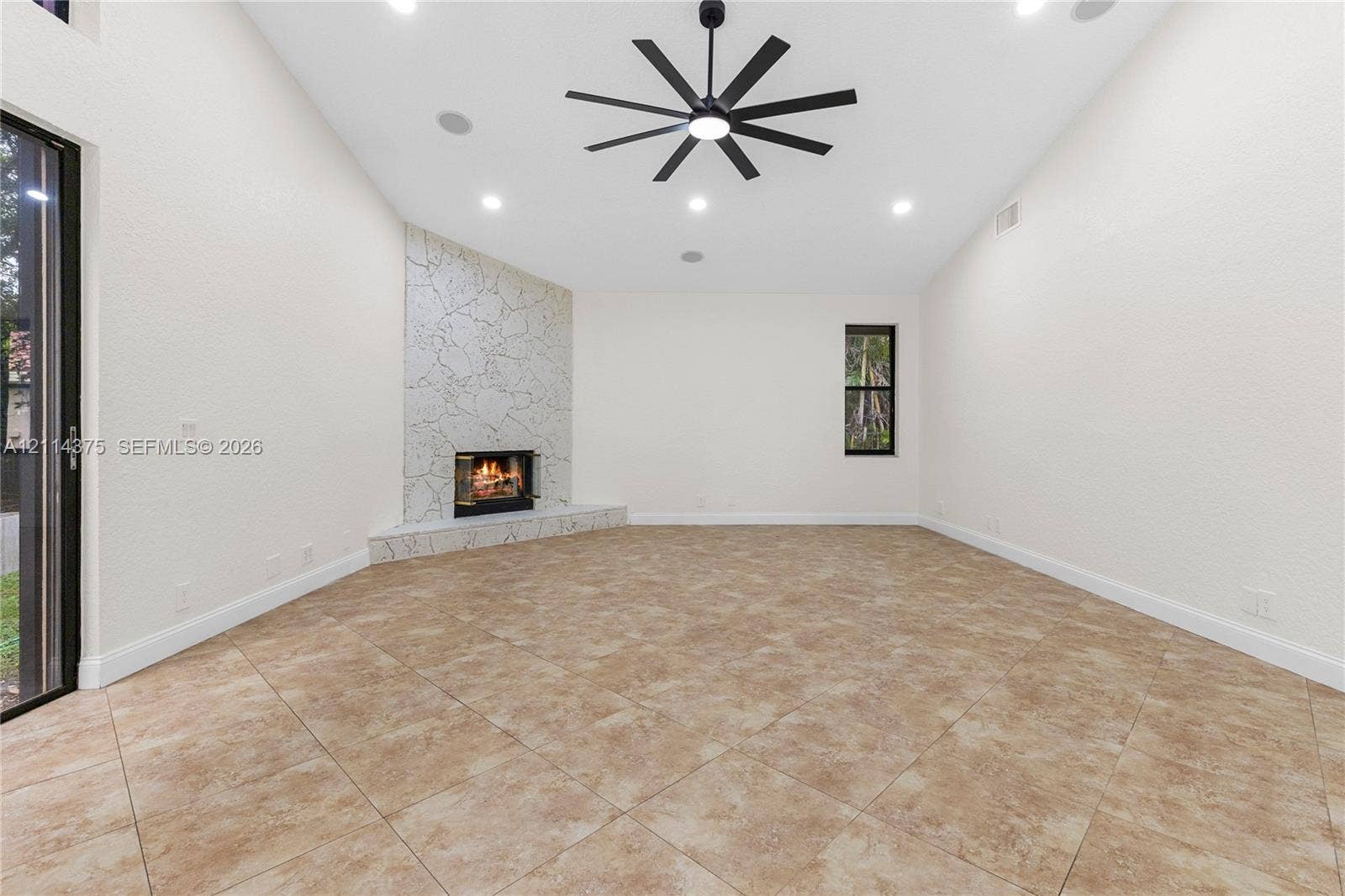 1206 S Manor Drive S, Weston, Weston, FL 33326 High vaulted ceilings, tile flooring, stone-accented corner fireplace, multi-blade ceiling fan, and large-format sliding glass doors
