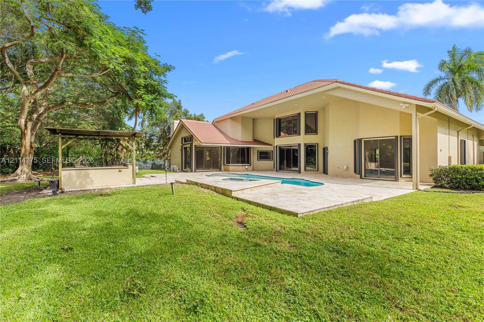 1206 S Manor Drive S, Weston, Weston, FL 33326 Rear exterior featuring a swimming pool, stone-paver patio, built-in outdoor bar, and manicured lawn with mature trees