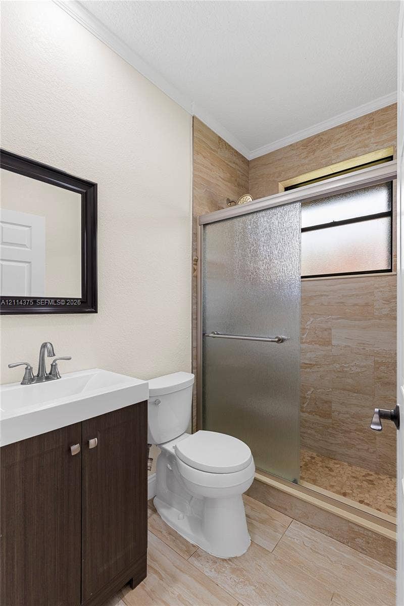1206 S Manor Drive S, Weston, Weston, FL 33326 Bathroom featuring a dark wood-finish vanity, integrated rectangular sink, brushed chrome fixtures, stone-style tiled shower enclosure with sliding glass door, and neutral tile flooring