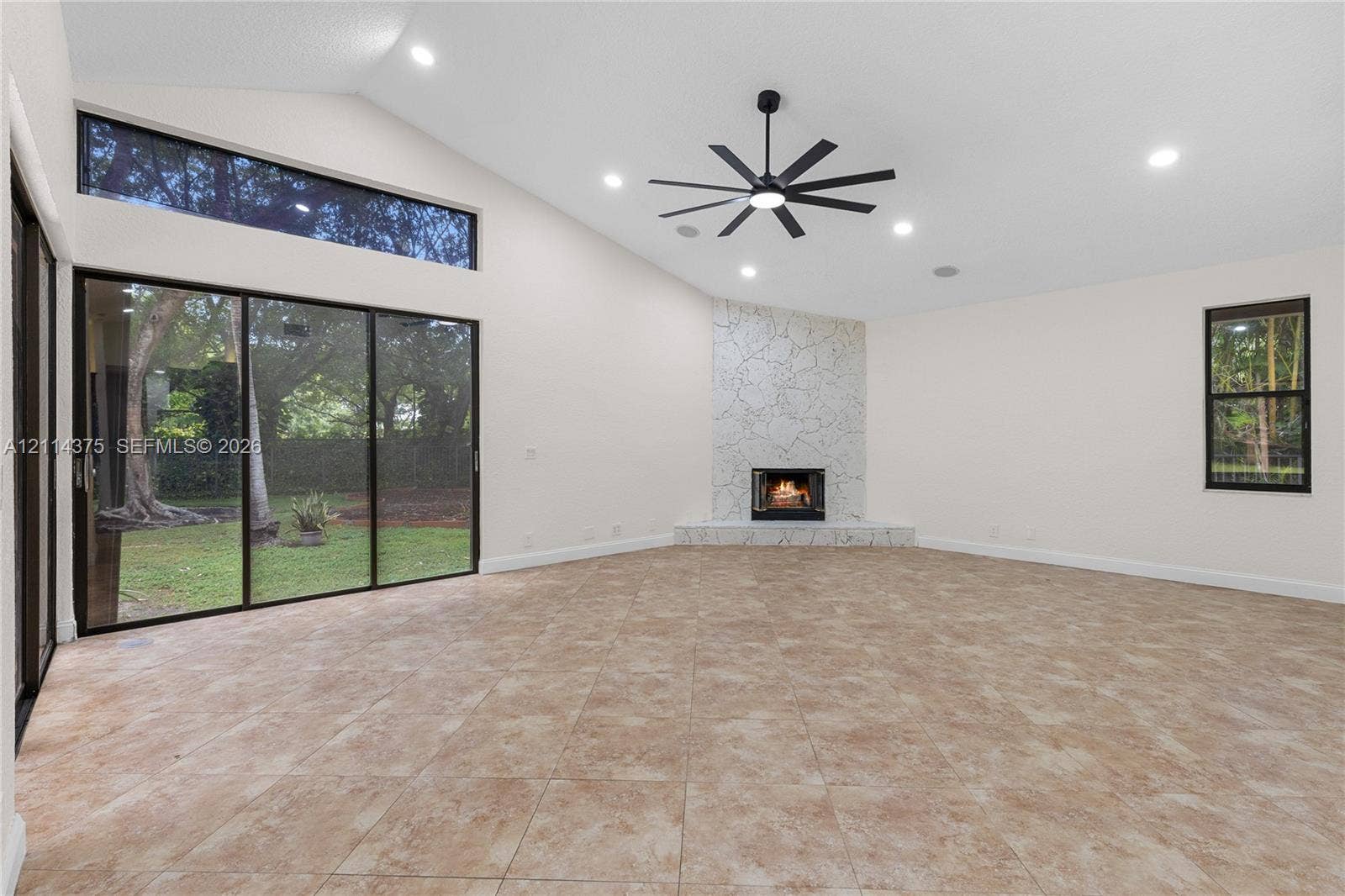 1206 S Manor Drive S, Weston, Weston, FL 33326 Vaulted ceilings featuring recessed lighting, expansive glass sliding doors, floor-to-ceiling stone-faced fireplace with a raised hearth, and neutral tile flooring