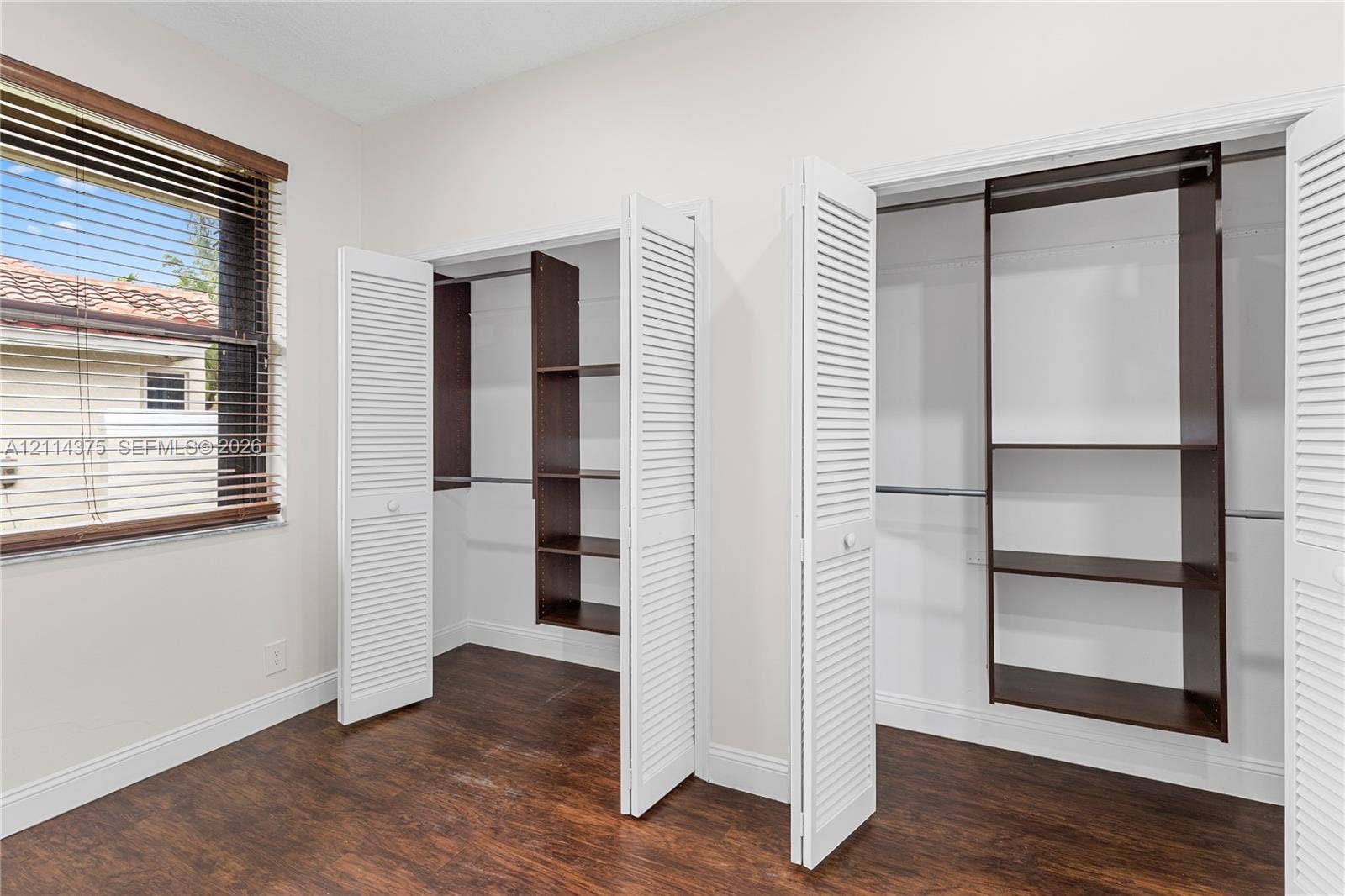 1206 S Manor Drive S, Weston, Weston, FL 33326 Wood-finish flooring, dual closets with white louvered doors, and built-in dark wood shelving units with integrated hanging rods