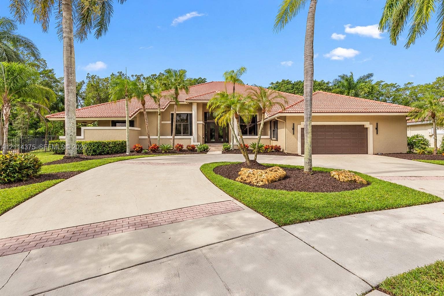 1206 S Manor Drive S, Weston, Weston, FL 33326 Stucco exterior featuring a terracotta-tile roof, expansive concrete driveway with brick inlay, and mature palm landscaping