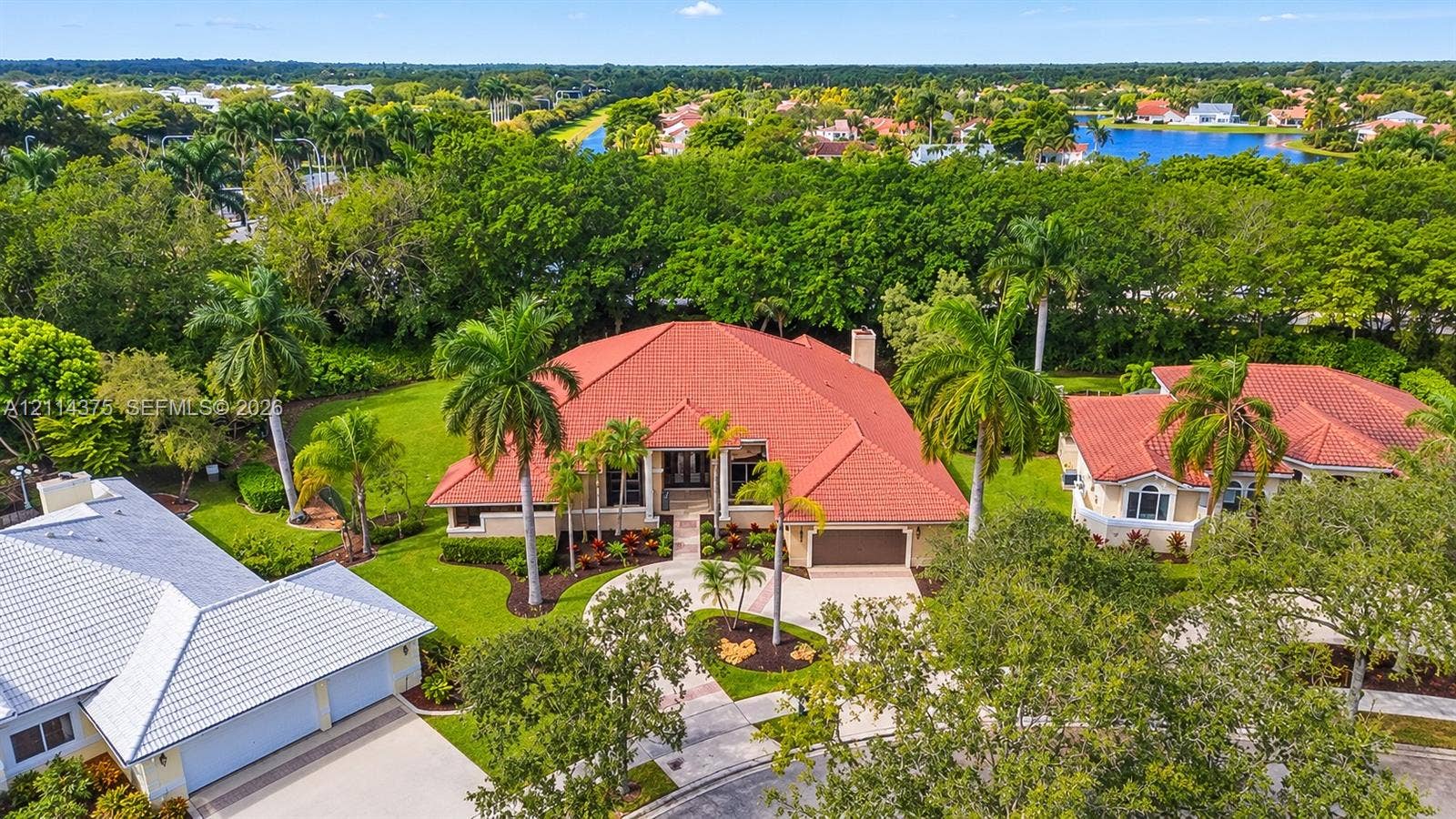 1206 S Manor Drive S, Weston, Weston, FL 33326 Aerial perspective featuring a multi-hipped clay tile roof, expansive manicured lawn, established palm landscaping, and concrete driveway