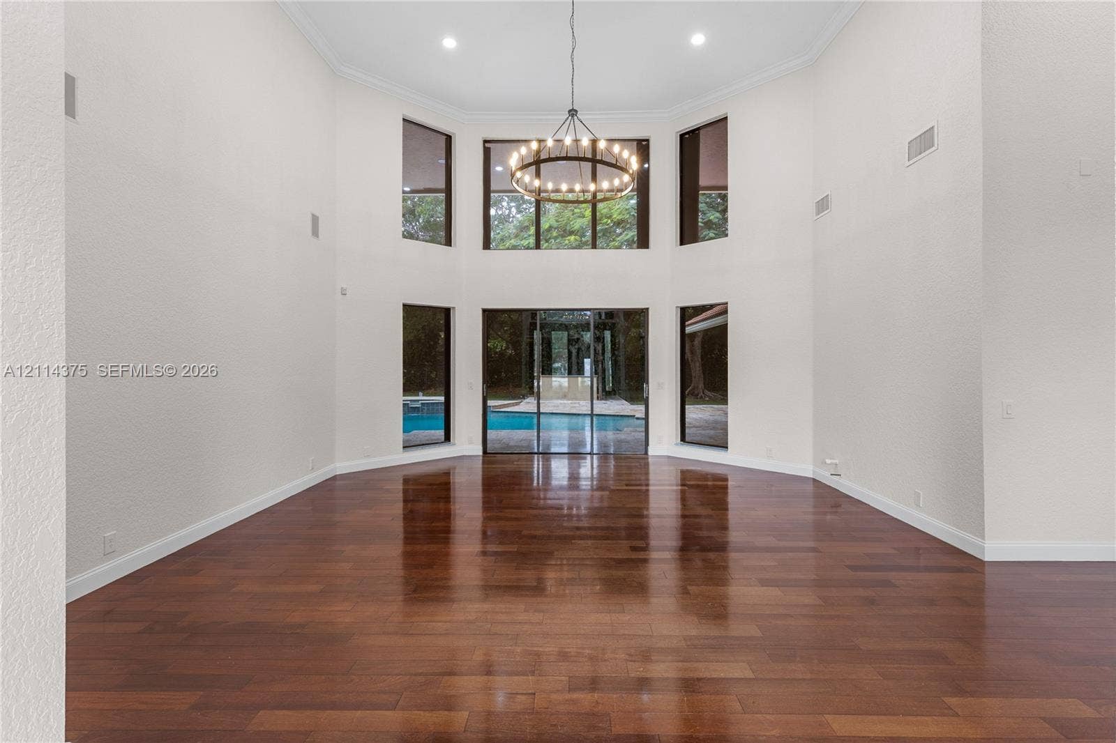 1206 S Manor Drive S, Weston, Weston, FL 33326 Expansive room featuring high ceilings, wood-finish flooring, floor-to-ceiling windows, a multi-tier circular chandelier, and sliding glass doors