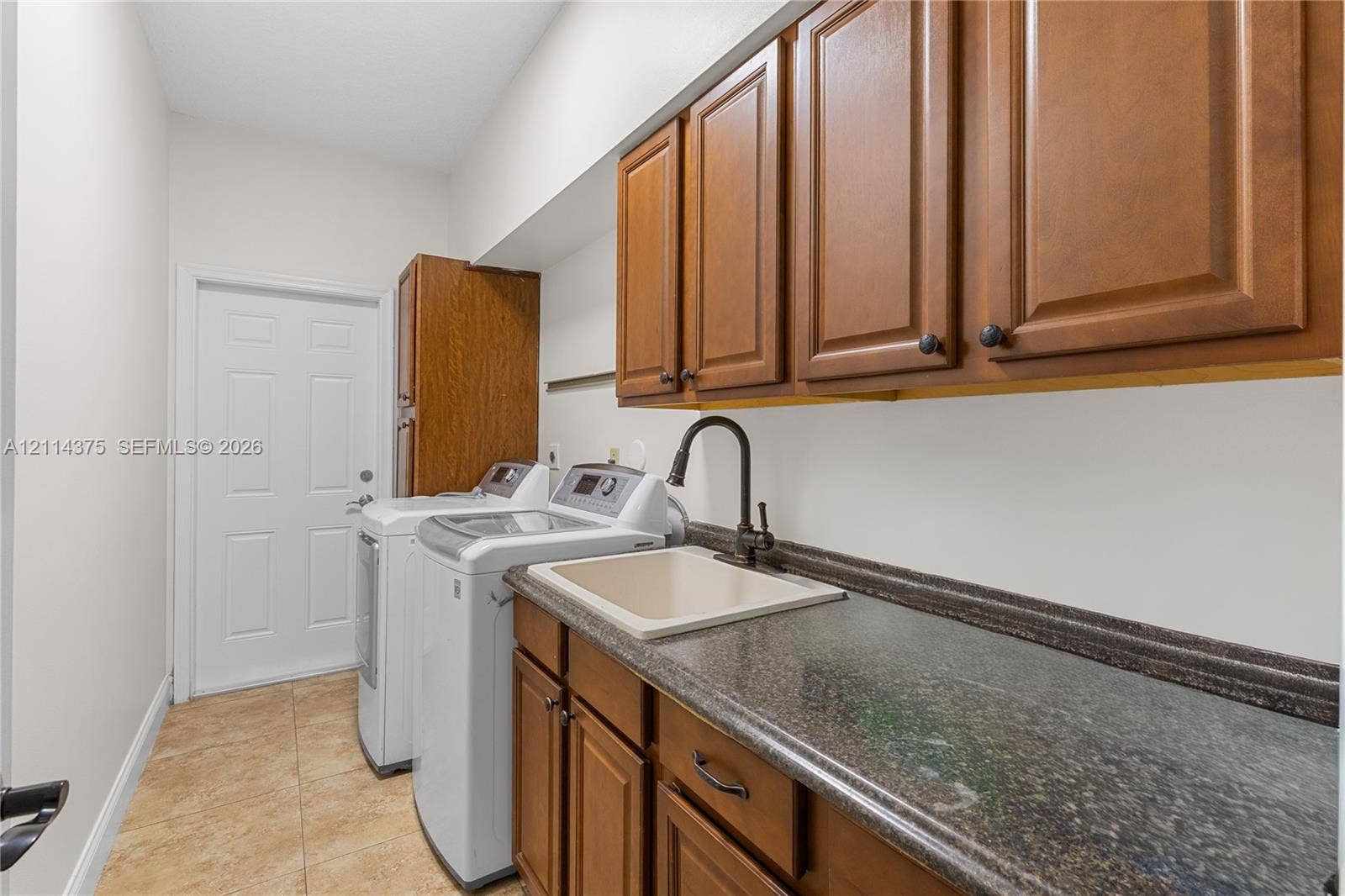 1206 S Manor Drive S, Weston, Weston, FL 33326 Laundry room featuring wood-finish cabinetry, stone-texture countertop, drop-in basin sink, matte black gooseneck faucet, and tile flooring
