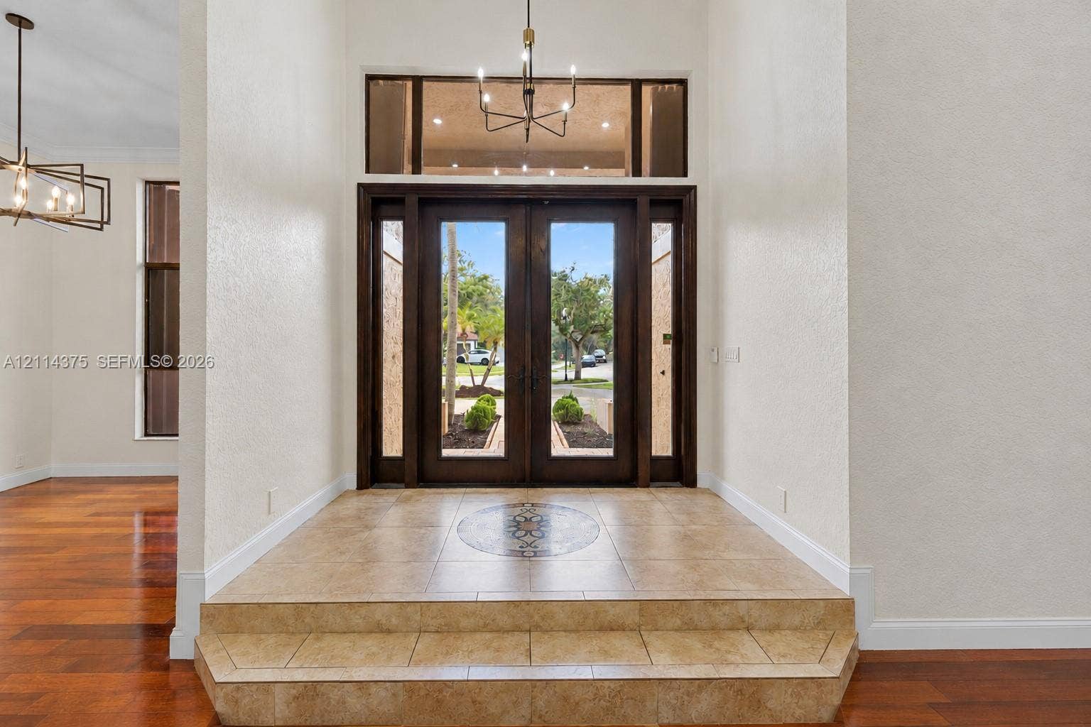 1206 S Manor Drive S, Weston, Weston, FL 33326 Entryway featuring double glass-paneled doors, decorative tile inlay, stepped tile flooring, transom window, and multi-arm chandelier