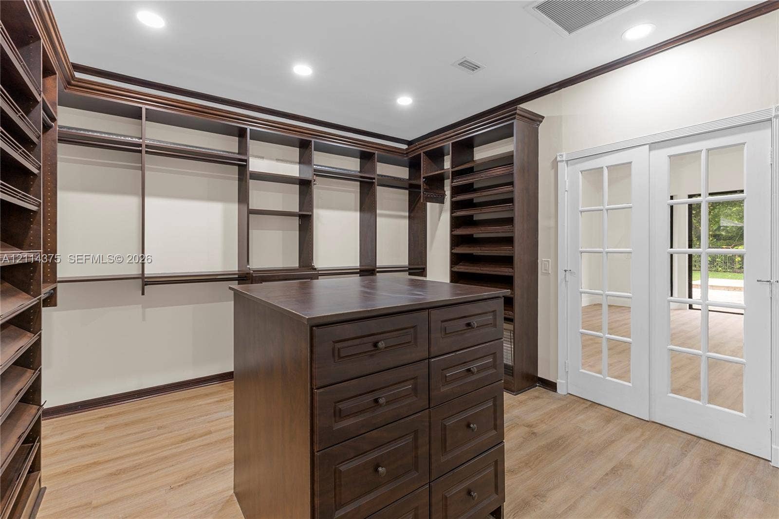 1206 S Manor Drive S, Weston, Weston, FL 33326 Custom storage cabinetry featuring extensive shelving, a central island with integrated drawers, wood-finish flooring, recessed lighting, and white French doors