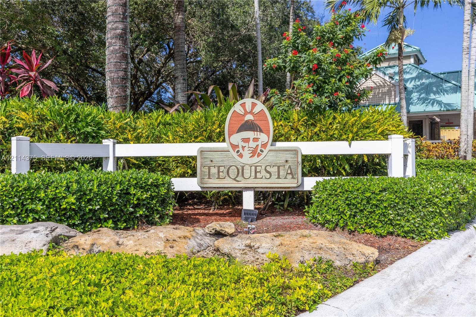 1206 S Manor Drive S, Weston, Weston, FL 33326 Community signage featuring custom wooden inlay, framed by a white post-and-rail fence, manicured hedges, and mature tropical landscaping