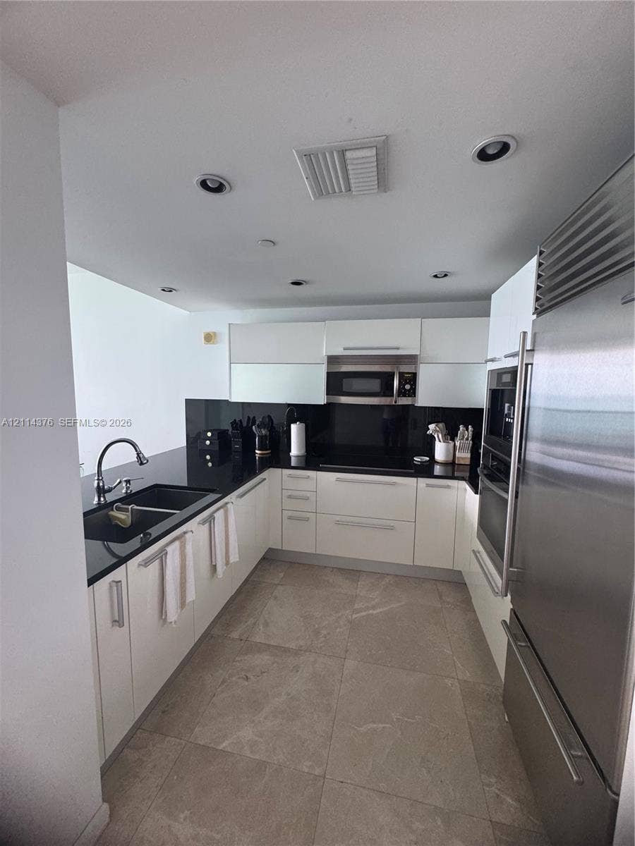 Kitchen featuring white cabinetry, black stone countertops, high-end stainless steel appliances, integrated cooktop, and large-format tile flooring