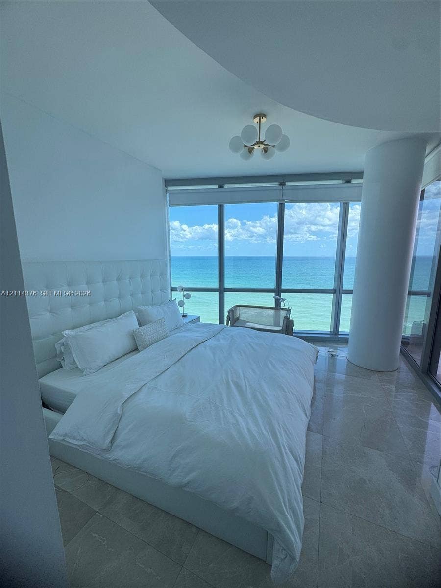Floor-to-ceiling windows featuring ocean scenery, stone flooring, a structural column, and a multi-globe light fixture