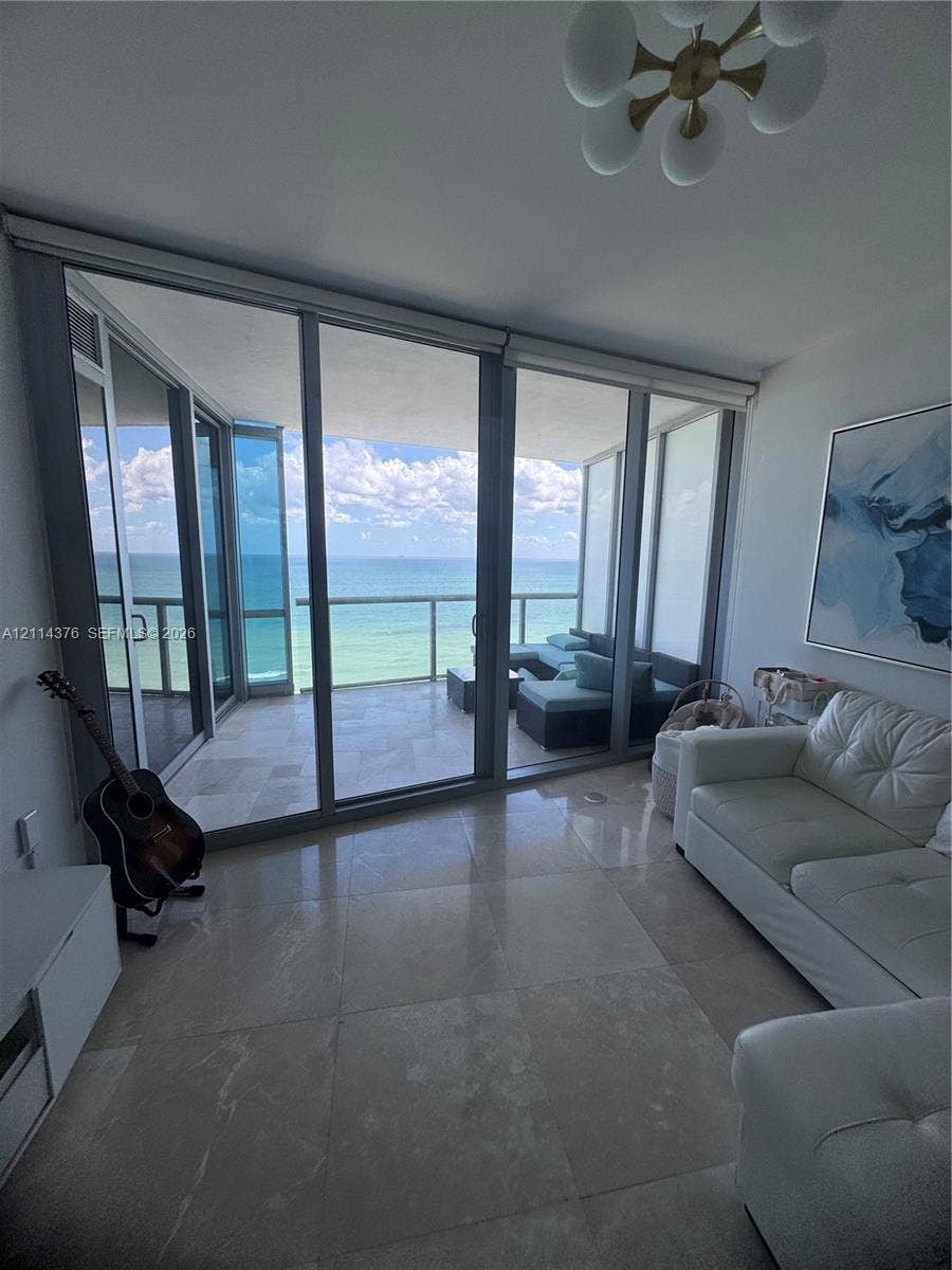 Floor-to-ceiling sliding glass doors, balcony with stone tile flooring, polished stone flooring, and multi-globe ceiling fixture
