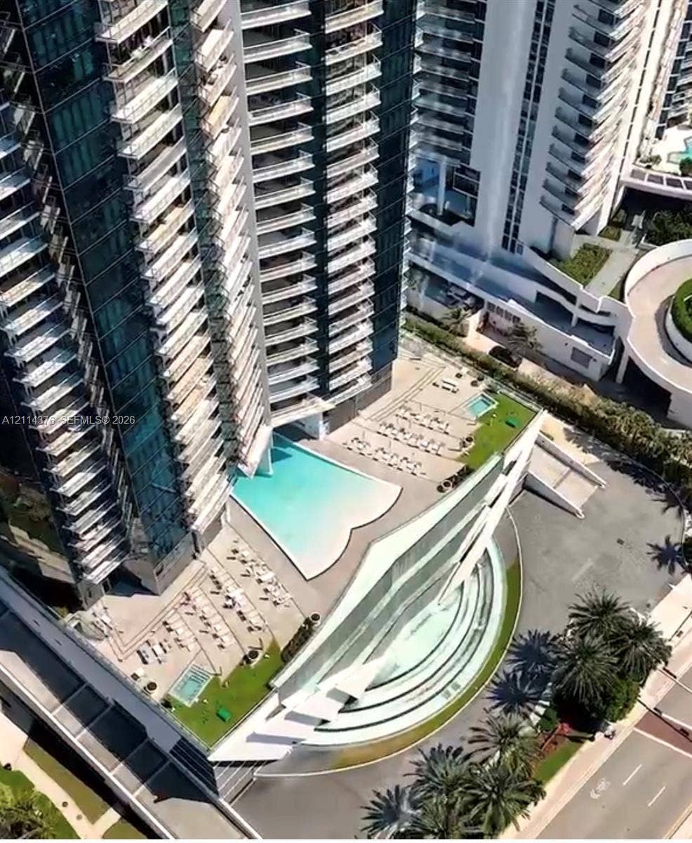 High-rise architectural exterior featuring tiered glass balconies, an expansive multilevel swimming pool area, multi-level terrace decks, and landscaped ground-level hardscaping