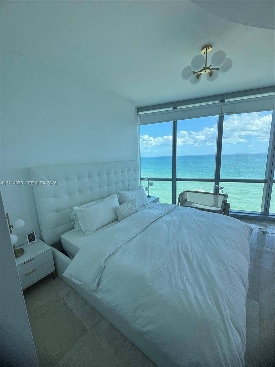 Floor-to-ceiling windows featuring ocean scenery, tile flooring, and a modern multi-globe chandelier