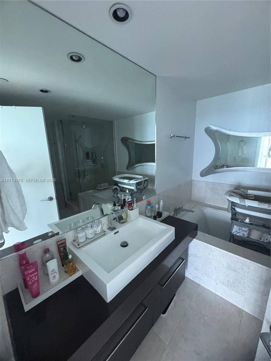 Contemporary bathroom featuring a dark-finish floating vanity, rectangular vessel sink, stone-surround soaking tub, and recessed ceiling lighting