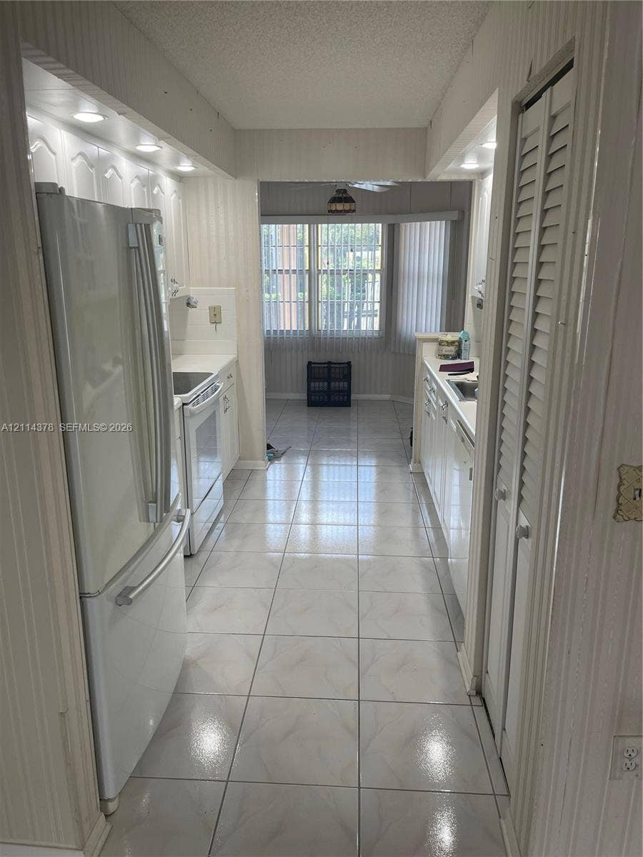 13355 SW 16th Court, #205E, Pembroke Pines, FL 33027 Galley-style kitchen featuring tile flooring, white cabinetry, integrated recessed lighting, and white appliances