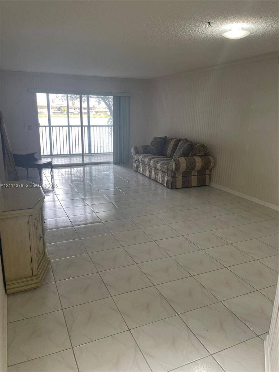 13355 SW 16th Court, #205E, Pembroke Pines, FL 33027 Large living area featuring neutral tile flooring, vertical wall paneling, and sliding glass doors with access to a railed balcony