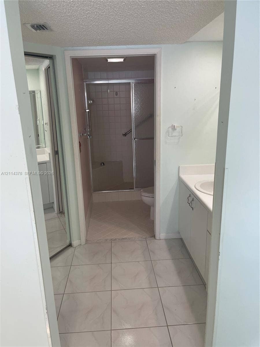 13355 SW 16th Court, #205E, Pembroke Pines, FL 33027 Bathroom featuring large-format ceramic tile flooring, white vanity cabinet with a solid surface countertop, integrated sink basin, and a walk-in shower with glass sliding doors