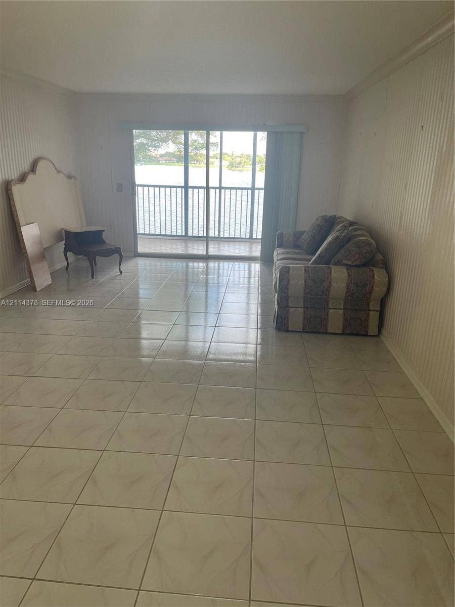 13355 SW 16th Court, #205E, Pembroke Pines, FL 33027 Interior space featuring light-toned ceramic tile flooring, vertical wall paneling, and large glass sliding doors leading to a screened balcony with water frontage
