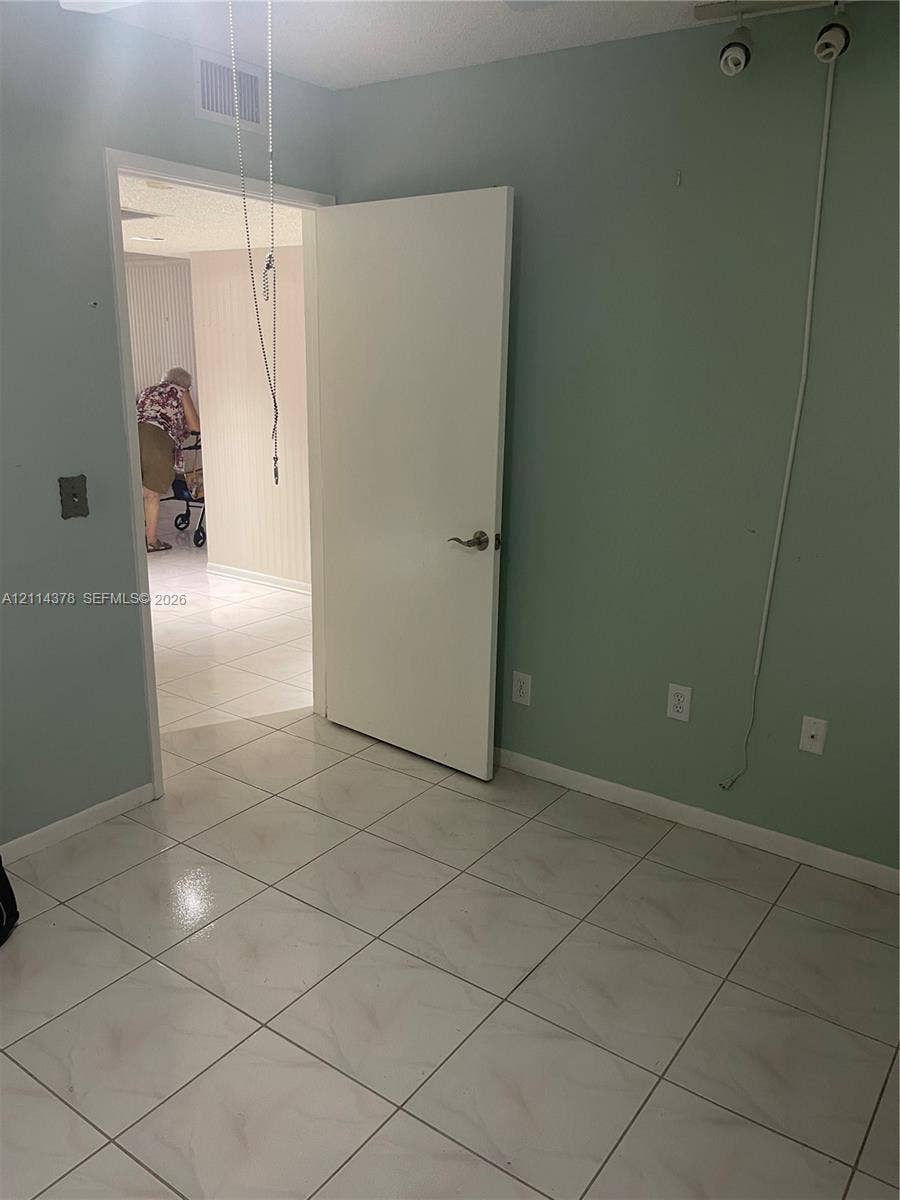 13355 SW 16th Court, #205E, Pembroke Pines, FL 33027 Room featuring large-format tile flooring, light green wall finishes, and a flush-mount interior door with metallic hardware