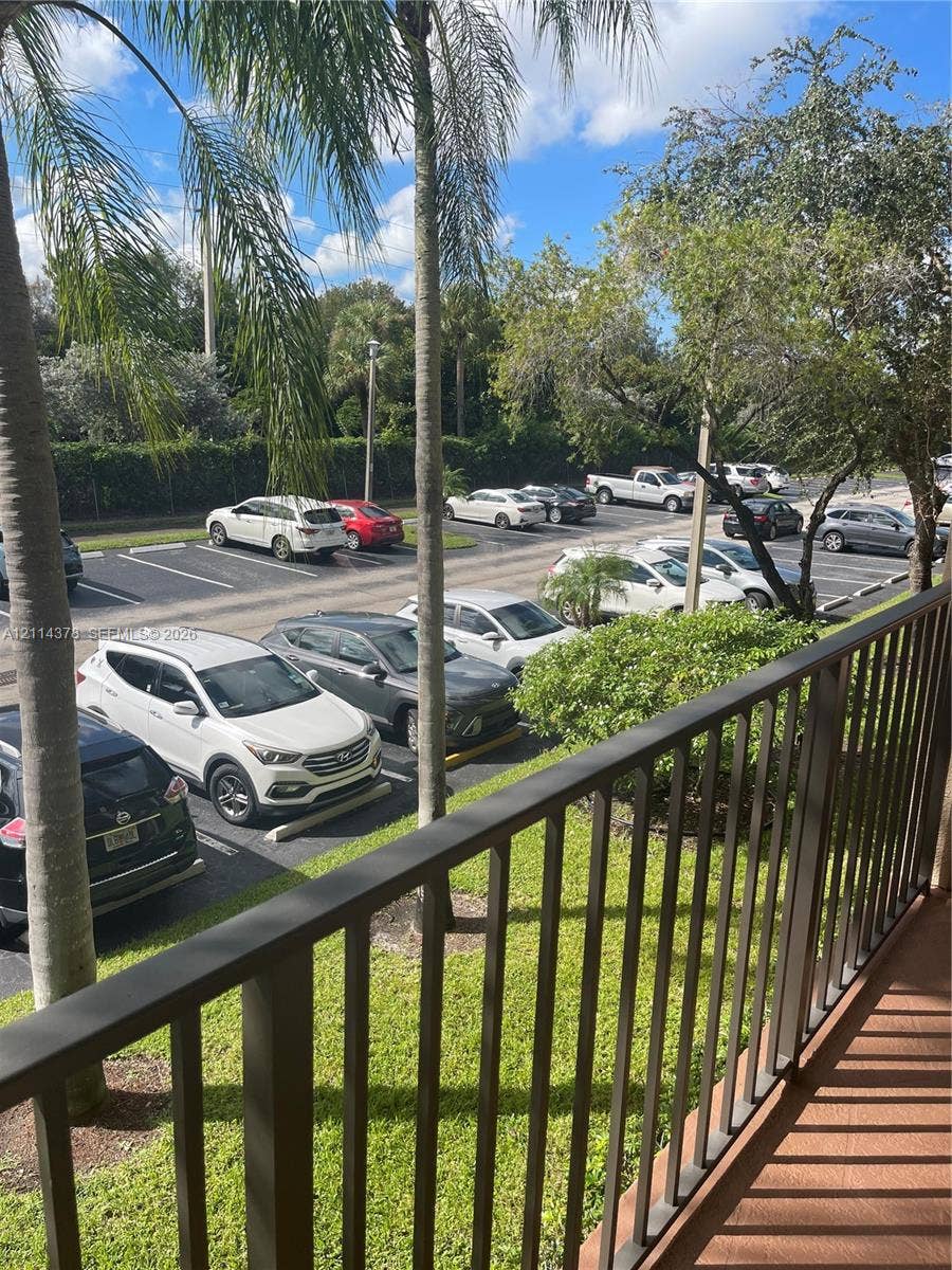 13355 SW 16th Court, #205E, Pembroke Pines, FL 33027 Balcony featuring a metal railing, overlooking a paved parking area with established palm trees and mature landscaping