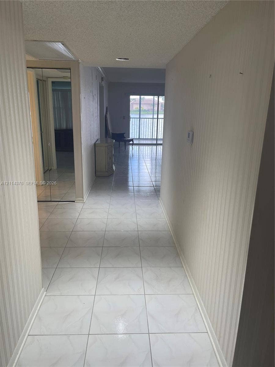 13355 SW 16th Court, #205E, Pembroke Pines, FL 33027 Interior corridor featuring large-format tile flooring, textured vertical wall surfacing, and mirrored sliding closet doors
