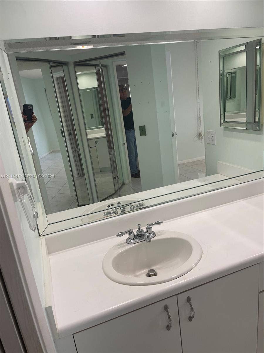 13355 SW 16th Court, #205E, Pembroke Pines, FL 33027 Vanity featuring a white countertop with an integrated oval sink, chrome dual-handle faucet, neutral cabinetry, and a full-width wall mirror with a beveled frame