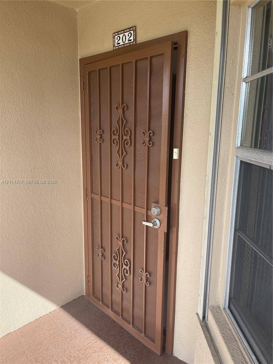 13355 SW 16th Court, #205E, Pembroke Pines, FL 33027 Brown metal security screen door featuring decorative scrollwork and a brushed-metal lever handle
