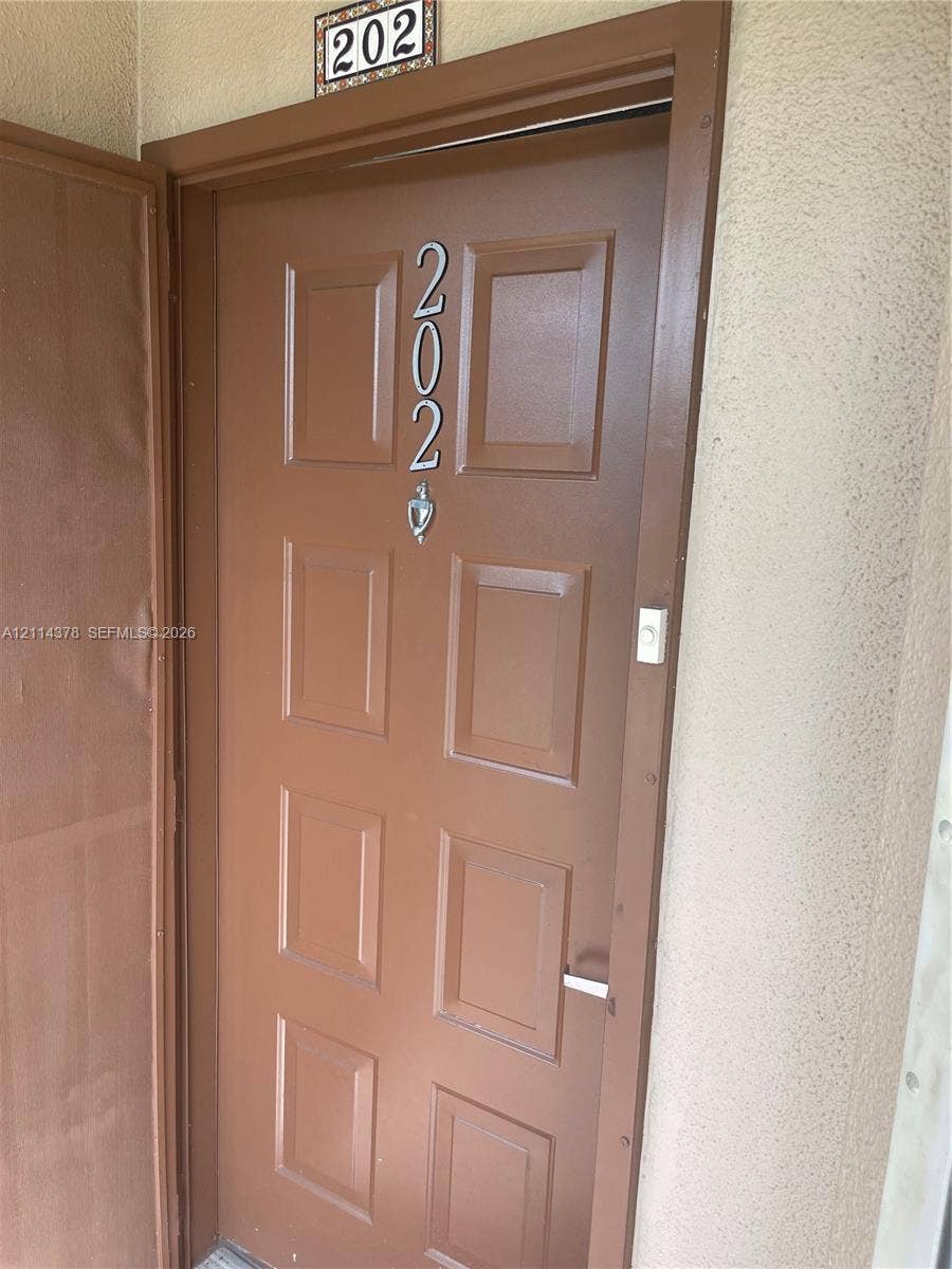 13355 SW 16th Court, #205E, Pembroke Pines, FL 33027 Solid-core door featuring eight recessed panels, metallic address numerals, a mounted door knocker, and an integrated doorbell