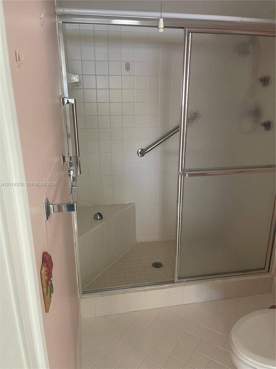 13355 SW 16th Court, #205E, Pembroke Pines, FL 33027 Walk-in shower featuring sliding glass doors, a built-in corner seat, tile surround, and chrome grab bars