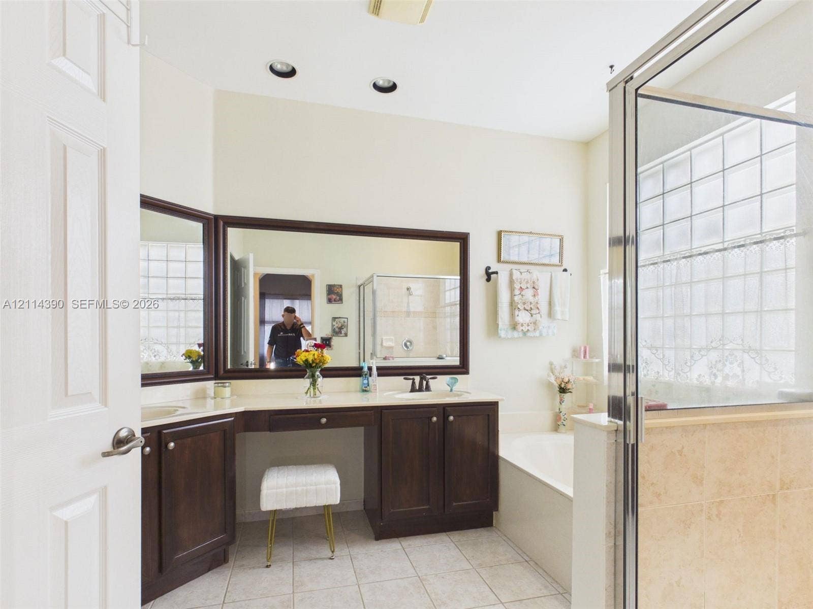 21196 Via Ventura, Boca Raton, FL 33433 Bathroom featuring a dual-sink vanity with dark wood cabinetry, large framed mirrors, a separate soaking tub, and a glass-enclosed shower with tiled surround