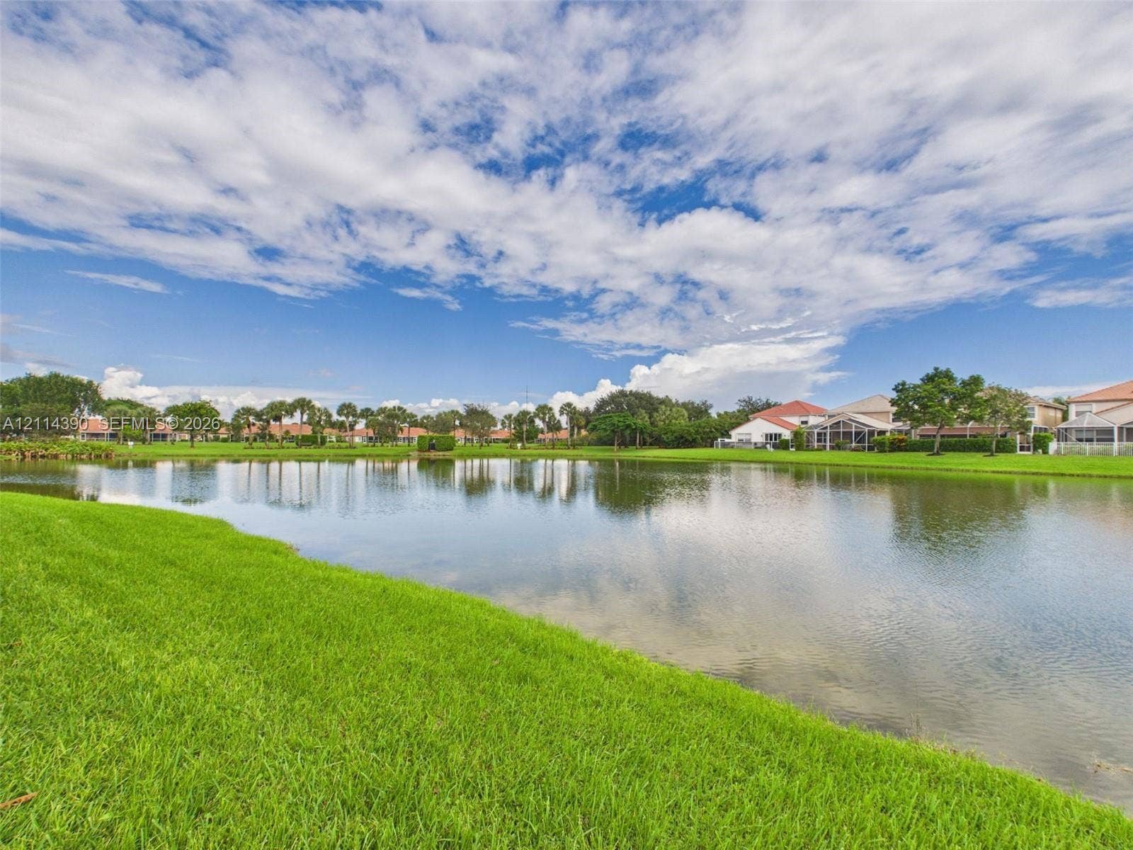 21196 Via Ventura, Boca Raton, FL 33433 Waterfront property featuring a manicured lawn, mature trees, and natural landscaping