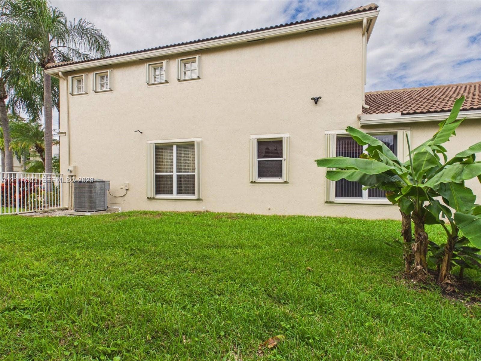 21196 Via Ventura, Boca Raton, FL 33433 Stucco exterior featuring a tile roof, multiple multi-pane windows, and an outdoor HVAC unit, set against a manicured lawn