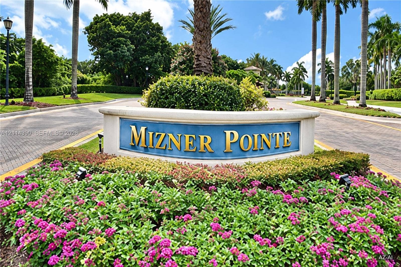 21196 Via Ventura, Boca Raton, FL 33433 Mizner Pointe community entrance featuring a curved stone-finish monument sign, paved roadway, mature palm trees, and professional landscaping with flowering shrubbery
