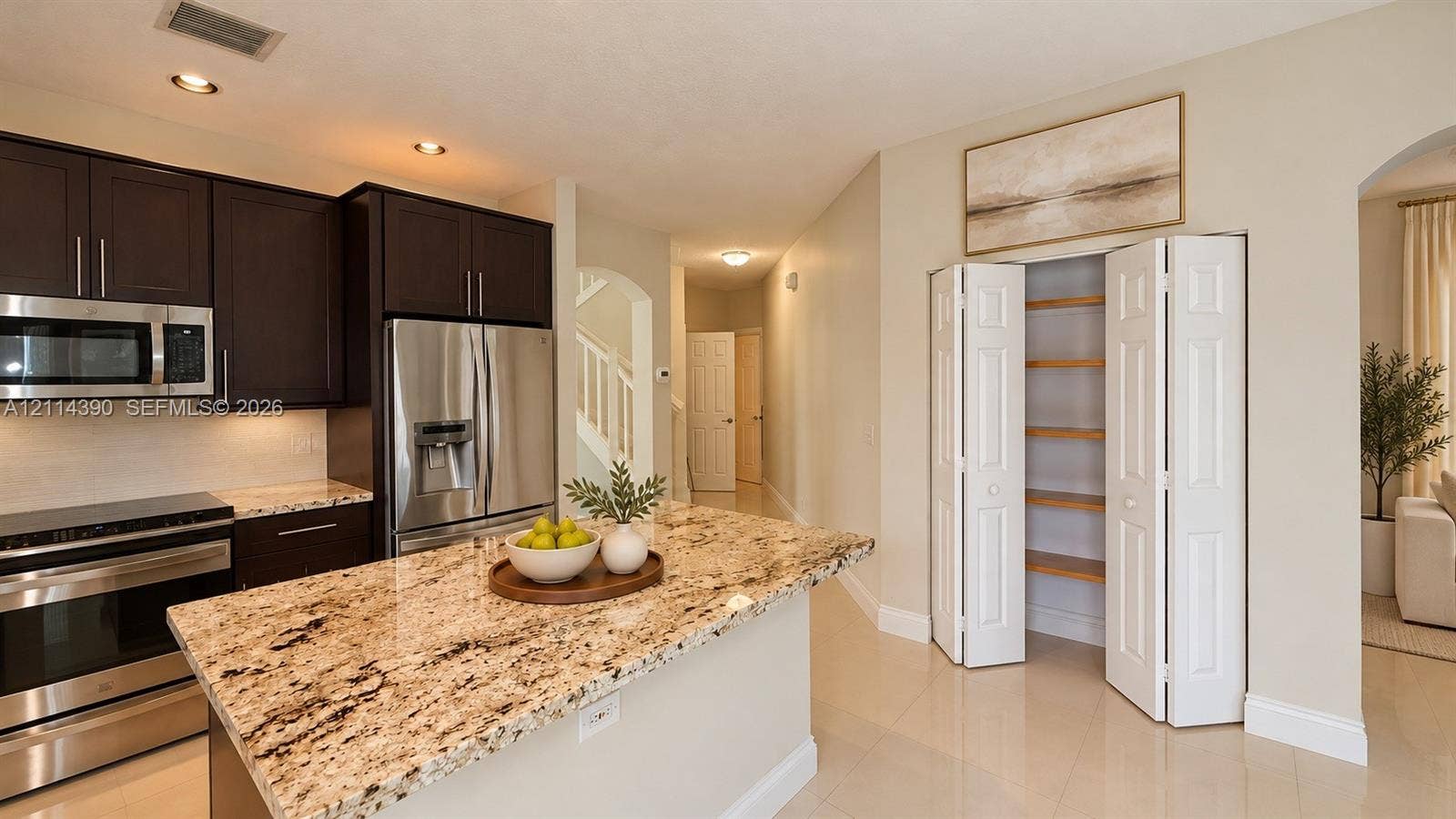 21196 Via Ventura, Boca Raton, FL 33433 Kitchen featuring dark cabinetry, stone countertops, stainless steel appliances, a center island, and a built-in pantry with bi-fold doors