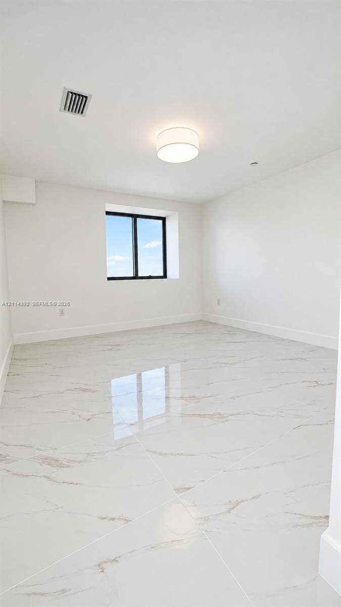 Large-format polished stone flooring with neutral veining, high-contrast black-framed window, and circular flush-mount ceiling light