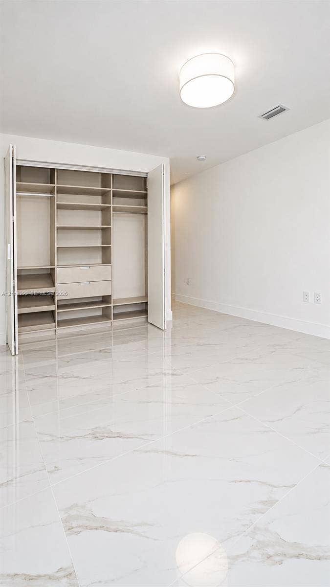 Large-format white tile flooring with veining, built-in closet organization system with integrated drawers and shelving, and flush-mount drum ceiling light