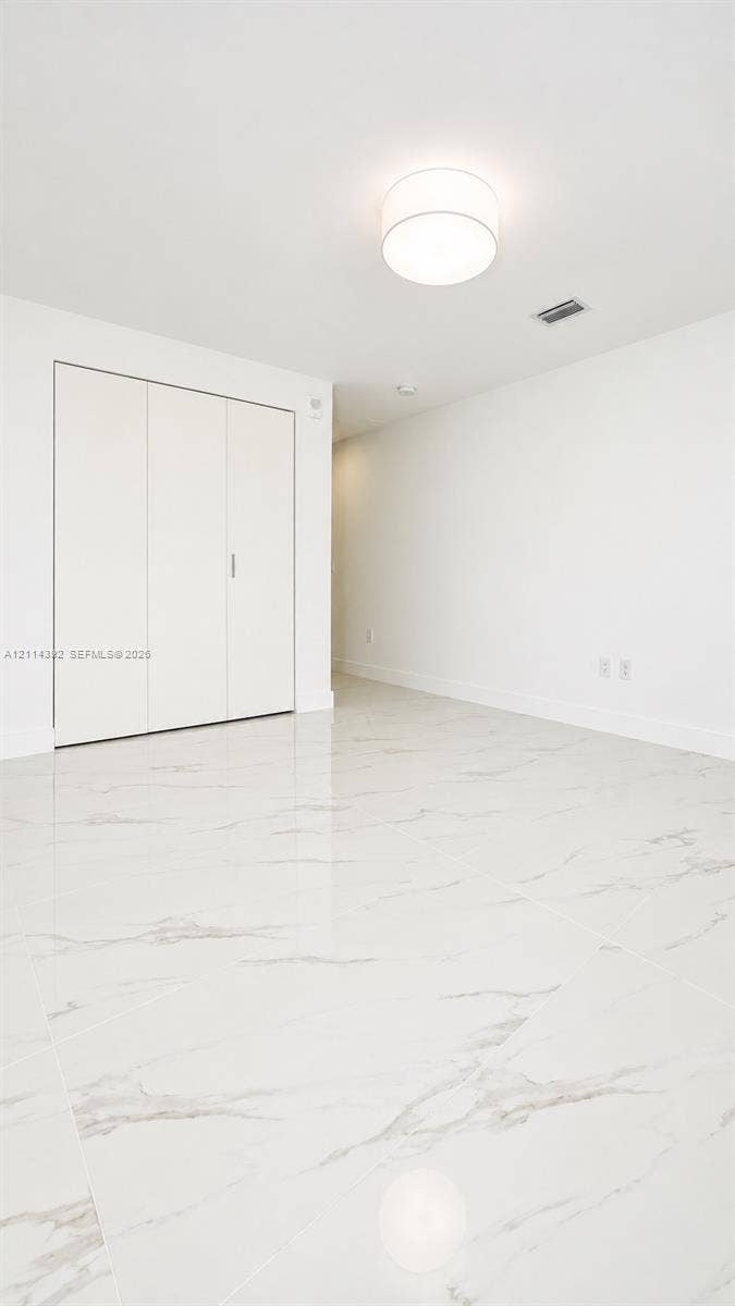 Polished stone-finish tile flooring, white walls, built-in closet with multi-panel doors, and a neutral drum-style ceiling fixture