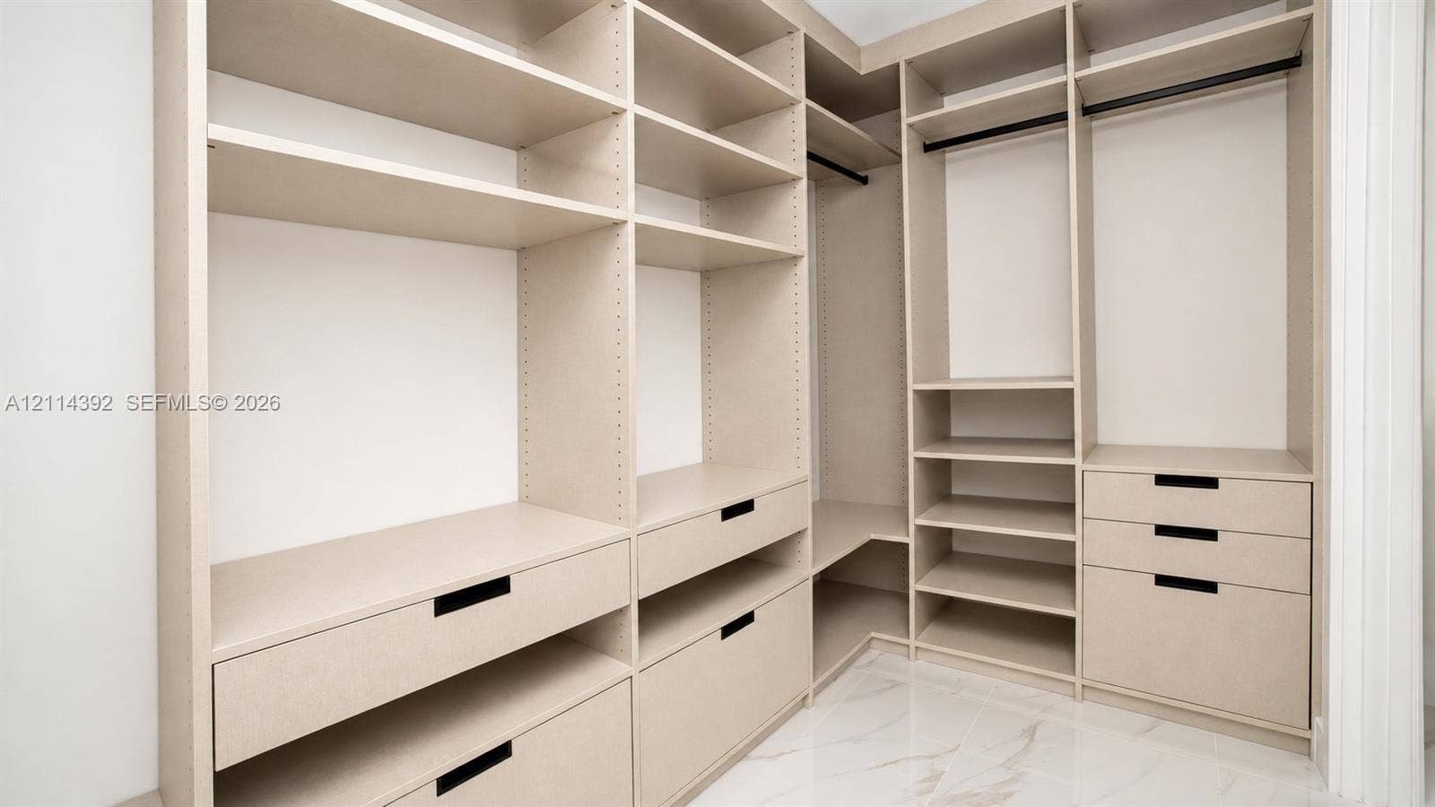 Custom walk-in closet featuring extensive built-in shelving, multiple integrated drawers with matte black pulls, dual hanging rods, and stone-finish flooring