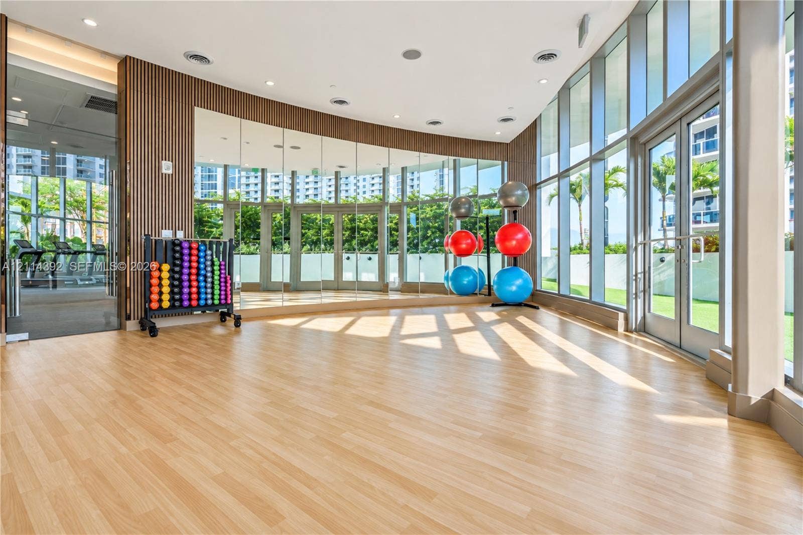 Fitness studio featuring floor-to-ceiling glass walls, wood-finish flooring, full-length mirror wall, and wood slat accent wall