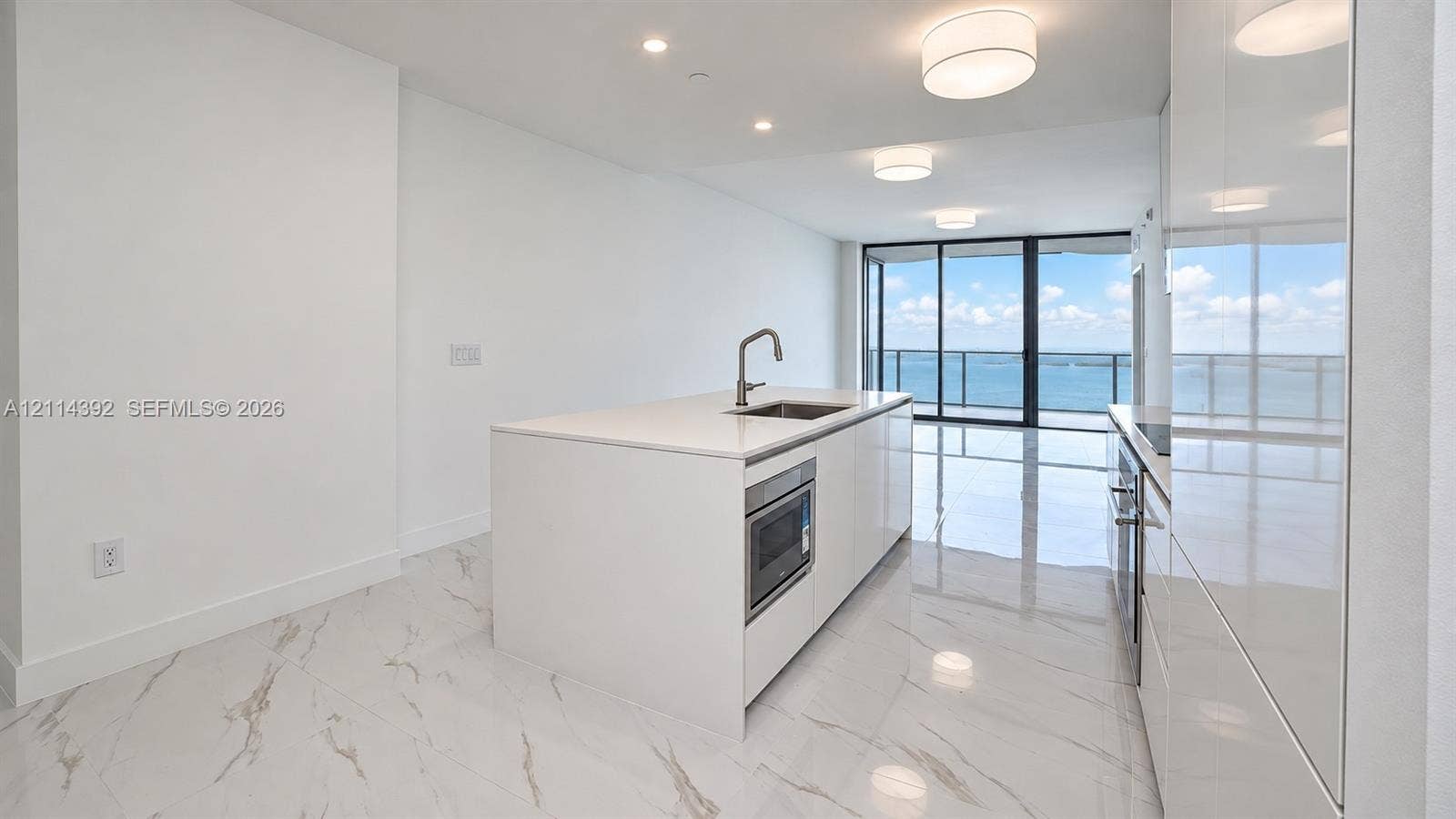 Kitchen featuring a central island with a quartz countertop, integrated microwave, undermount stainless steel sink, sleek high-gloss cabinetry, and light-toned tile flooring
