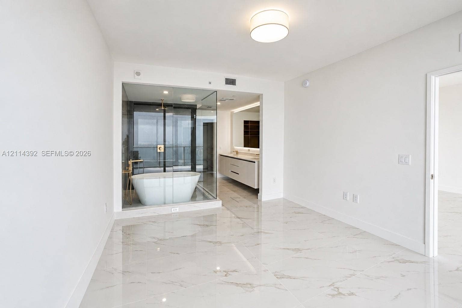 Polished stone-finish flooring, glass-enclosed bathroom area featuring a freestanding soaking tub, dual-sink floating vanity, and flush-mount lighting
