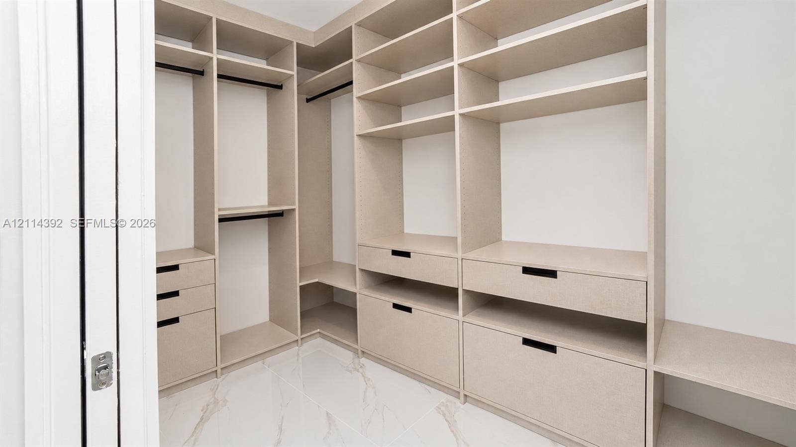 Custom walk-in closet featuring extensive built-in shelving, integrated storage drawers, hanging rods, and large-format tile flooring