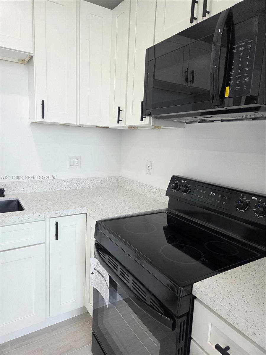 401 Pembroke Road, #202, Hallandale Beach, Hallandale Beach, FL 33009 White Shaker-style cabinetry with matte black hardware, stone-composite countertops, built-in black over-the-range microwave, and matching black electric range