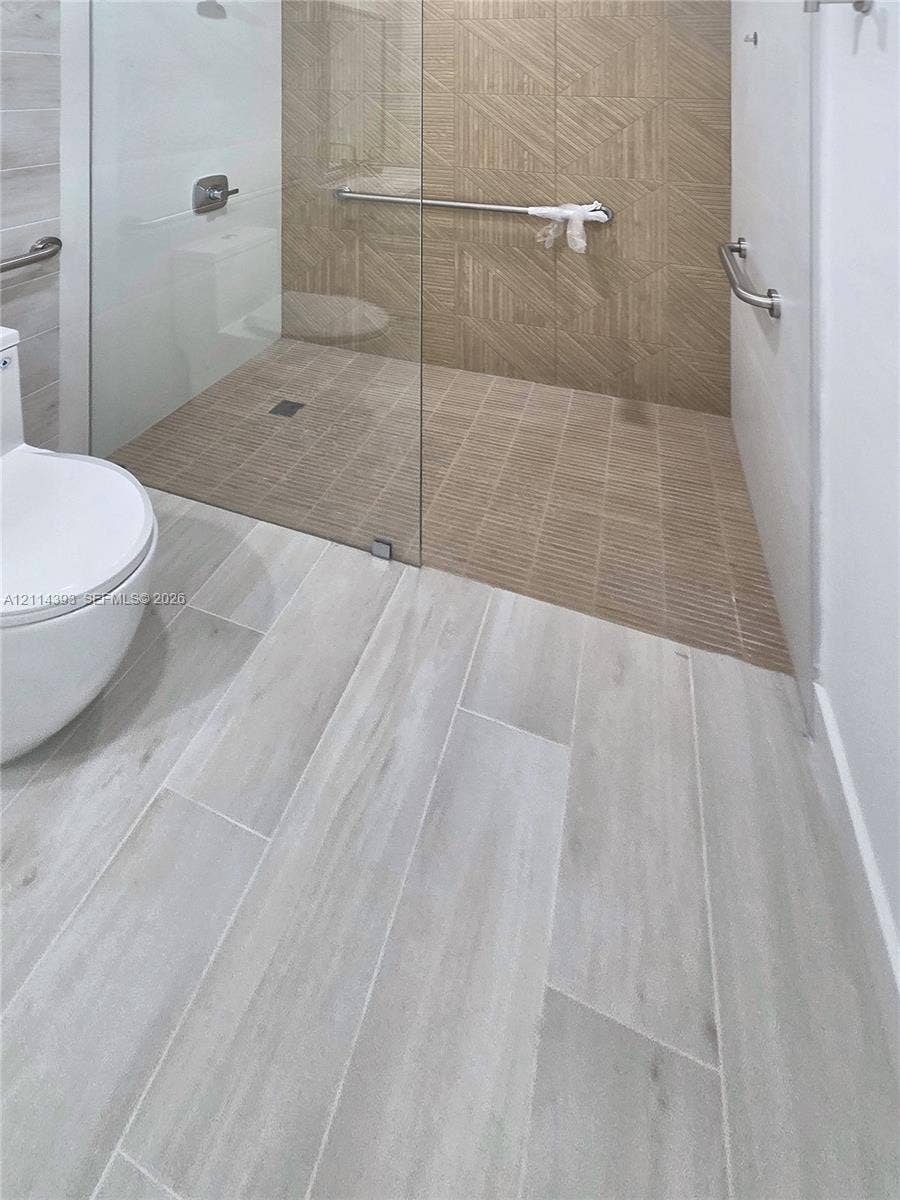 401 Pembroke Road, #202, Hallandale Beach, Hallandale Beach, FL 33009 Walk-in shower featuring a frameless glass enclosure, geometric-patterned tile wall accents, wood-finish floor tiling, and wall-mounted metal support bars