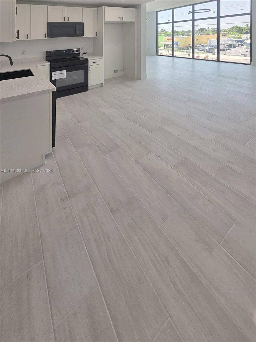 401 Pembroke Road, #202, Hallandale Beach, Hallandale Beach, FL 33009 Kitchen featuring white shaker-style cabinetry, solid-surface countertops, black integrated appliances, and wood-finish flooring, accented by floor-to-ceiling windows