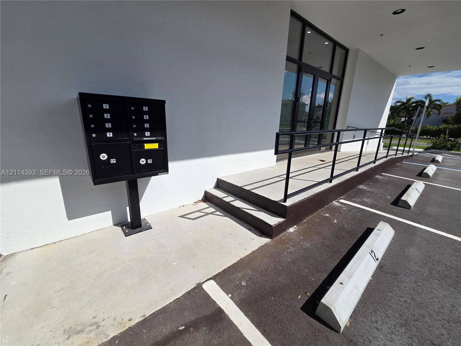 401 Pembroke Road, #202, Hallandale Beach, Hallandale Beach, FL 33009 Exterior entrance featuring a concrete ramp with black metal handrails, a multi-unit wall-mounted mailbox system, and marked parking spaces with concrete wheel stops
