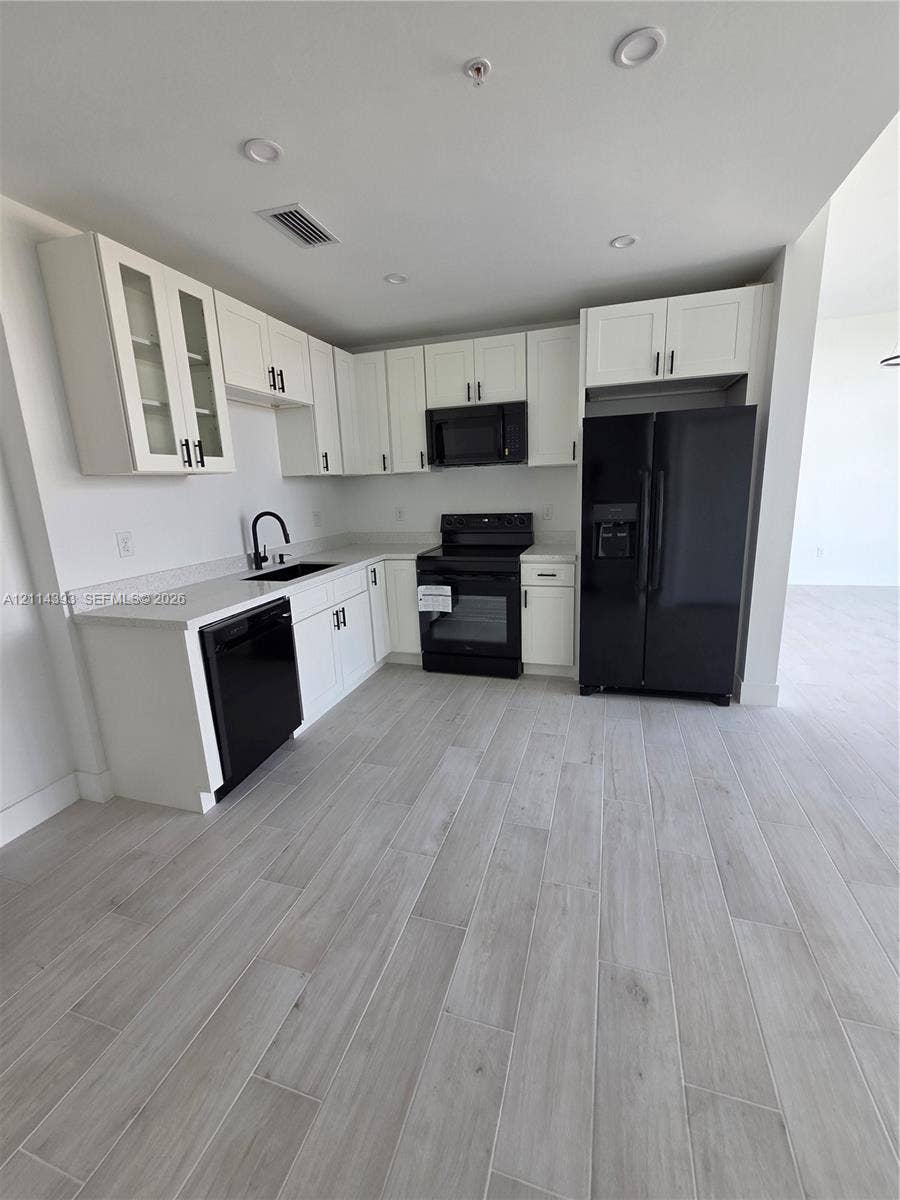 401 Pembroke Road, #202, Hallandale Beach, Hallandale Beach, FL 33009 Kitchen featuring white shaker-style cabinetry, quartz countertops, black appliances, a gooseneck faucet, and wood-finish tile flooring