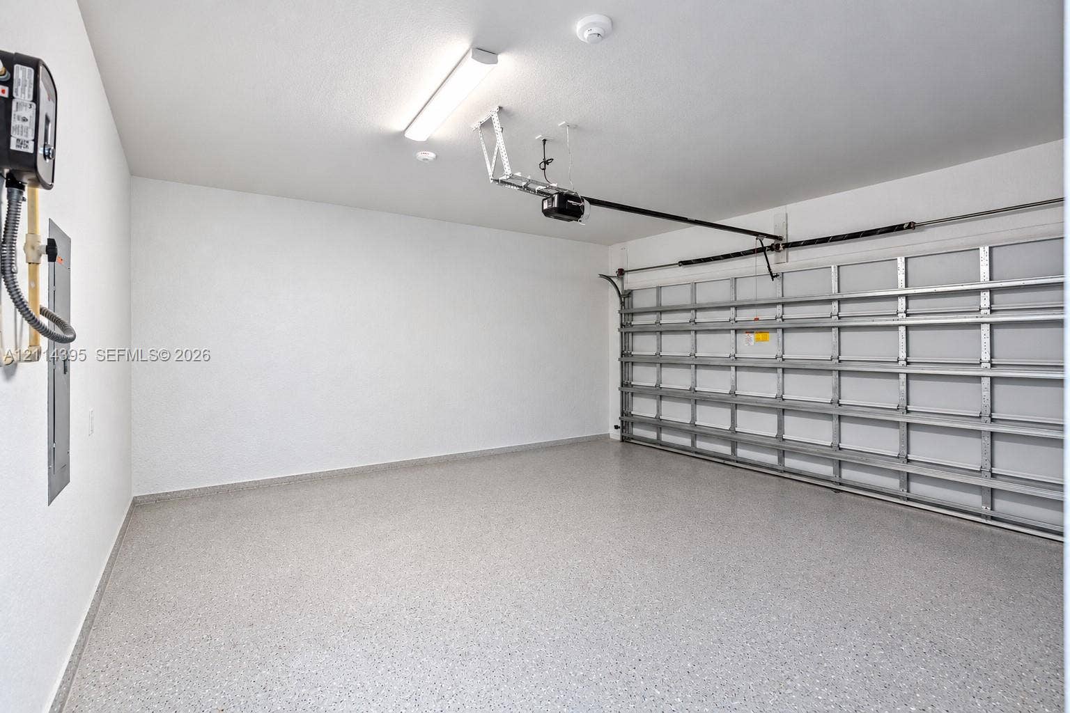 1615 NW 8th Avenue, Fort Lauderdale, FL 33311 Garage space featuring epoxy-coated flooring, smooth white walls, an automated door opener, and overhead fluorescent lighting