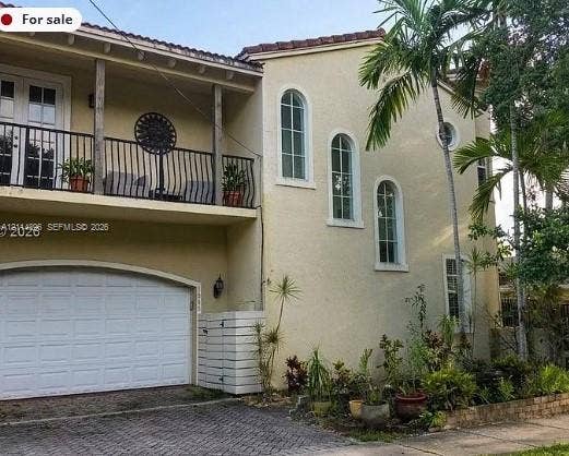 Fort Lauderdale, FL 33315 Stucco exterior featuring an arched-entry garage, wrought-iron railed upper balcony, barrel tile roofing, and arched windows