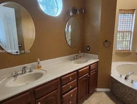 Fort Lauderdale, FL 33315 Dual-sink vanity with light-toned countertop, wooden cabinetry, oval wall-mounted mirrors, circular accent window, and jetted soaking tub featuring decorative tile surround